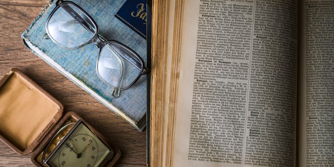 opengeslagen oud woordenboek met een leesbril ernaast